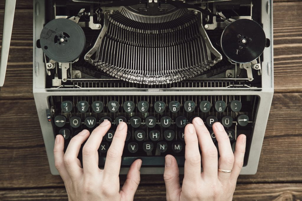 An image of a typewriter and hands typing.